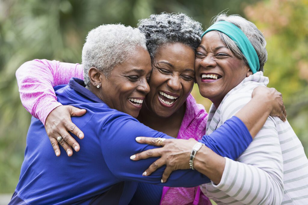 Three senior women at Porters Neck Village hugging and smiling