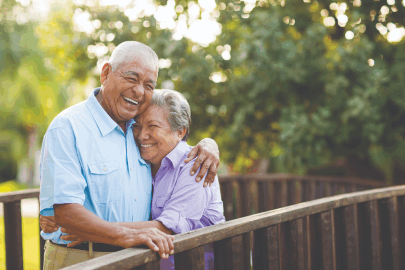 A senior couple smiling and hugging outside at Porters Neck Village.