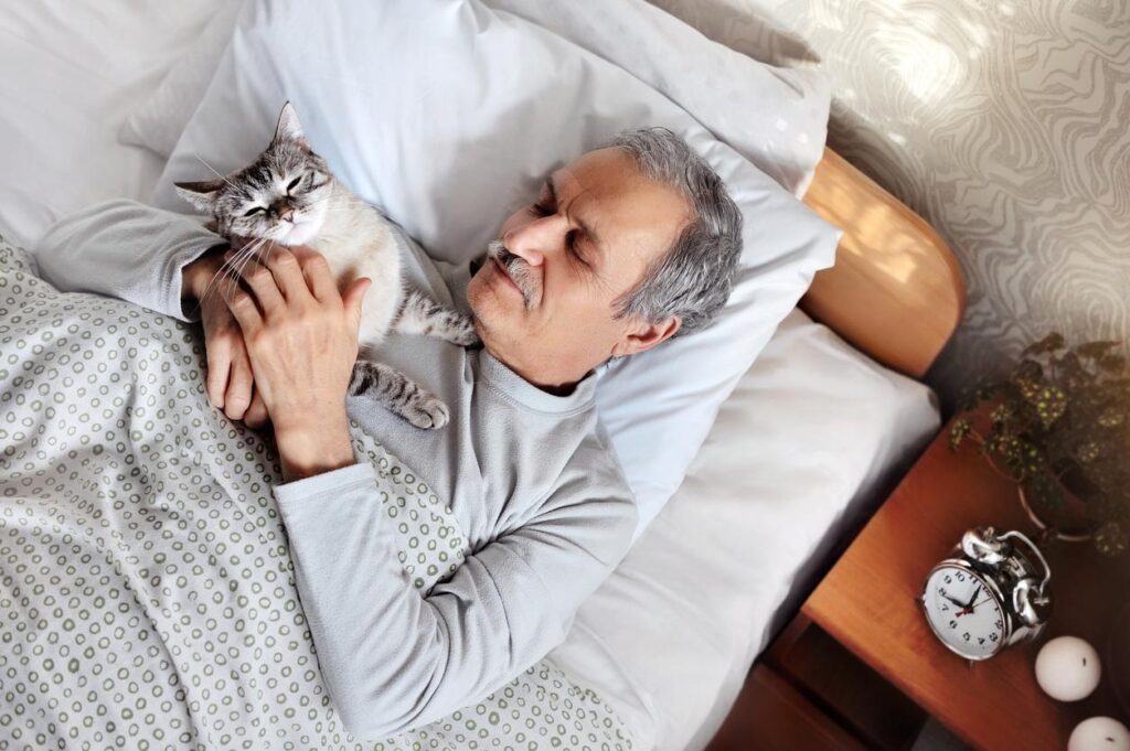 Mature man lies in bed snuggling his cat as they wake up for the day
